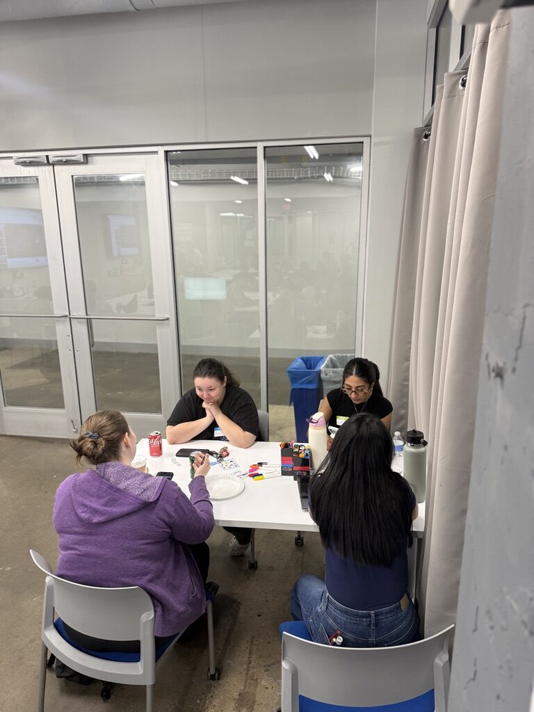 A small group works around a table by the glass wall, phones and NFC tags spread in front of them.