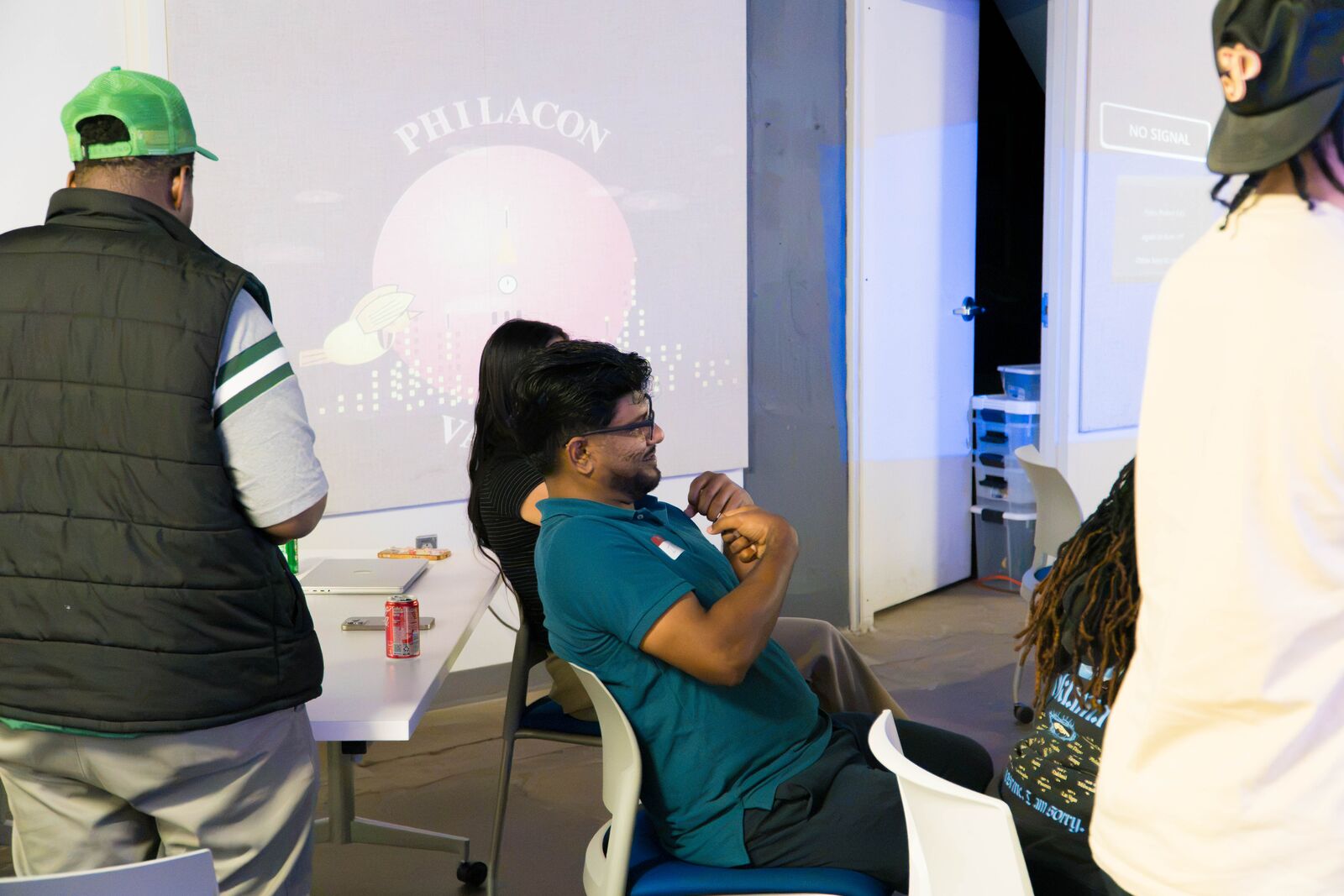 Attendees sit and stand in a darkened room in front of a large wall projection of PhilaCon Valley artwork.